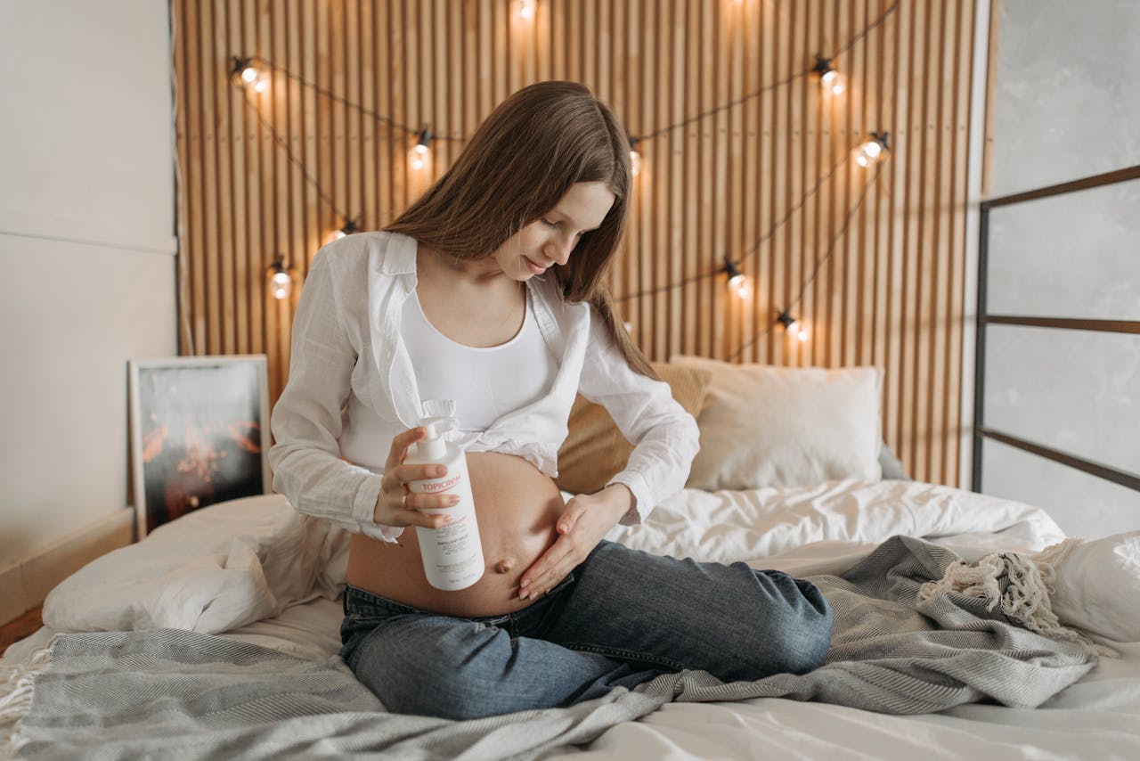 Expectant mother cares for her belly with lotion in a cozy bedroom setting.